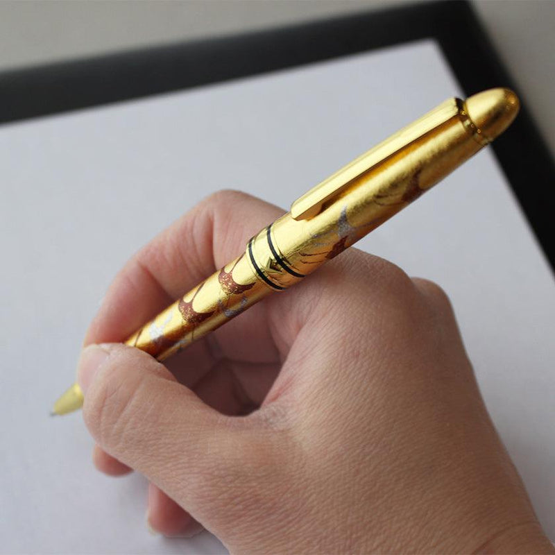 蒔絵ボールペン千羽鶴 金を手に持ちノートに書く様子、金沢箔仕上げの輝く軸が際立つ｜箔一