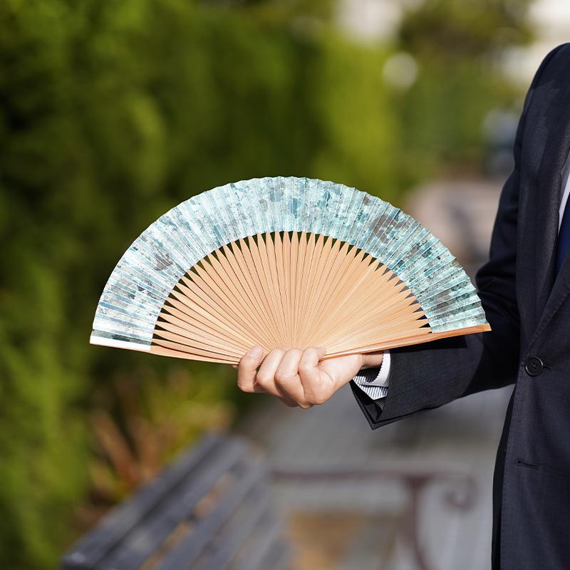 箔彩 hakuiro 水浅葱 7.5寸を手に持つ男性——水色の箔散らし文様が美しい京扇子｜京都府・米原康人
